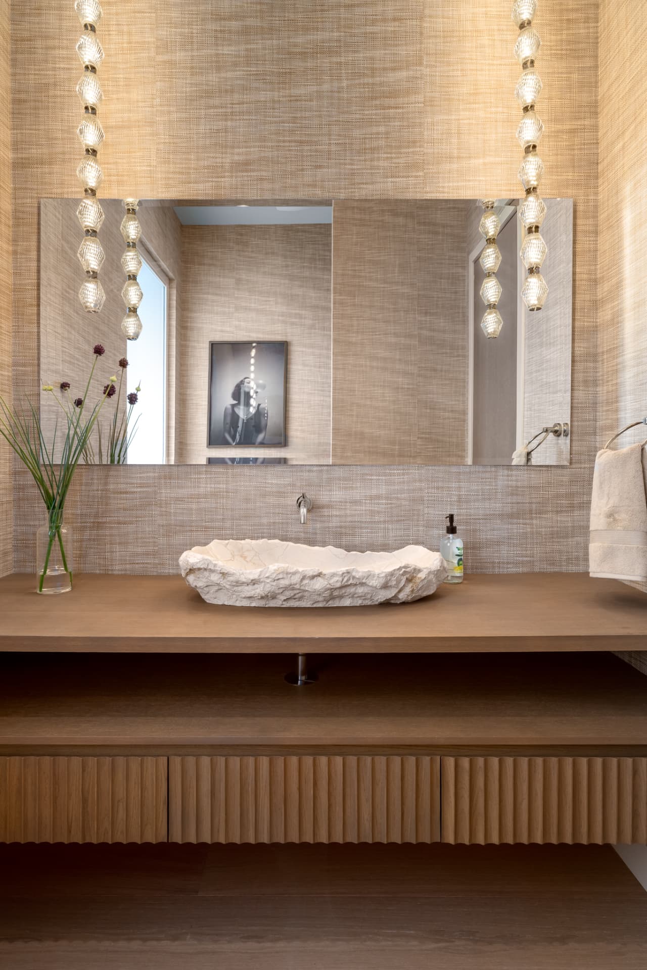 Powder bath with carved stone vessel sink, grasscloth walls and designer pendants