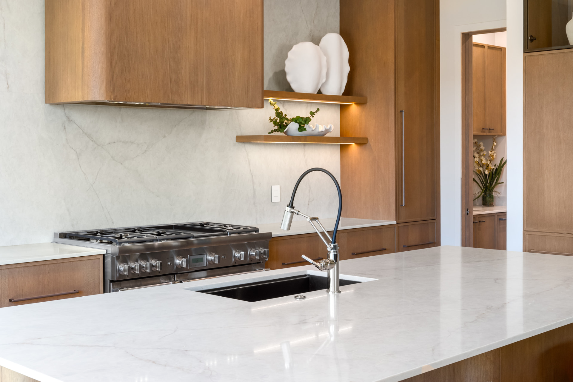 Kitchen detail with professional range, marble backsplash and lit floating shelves