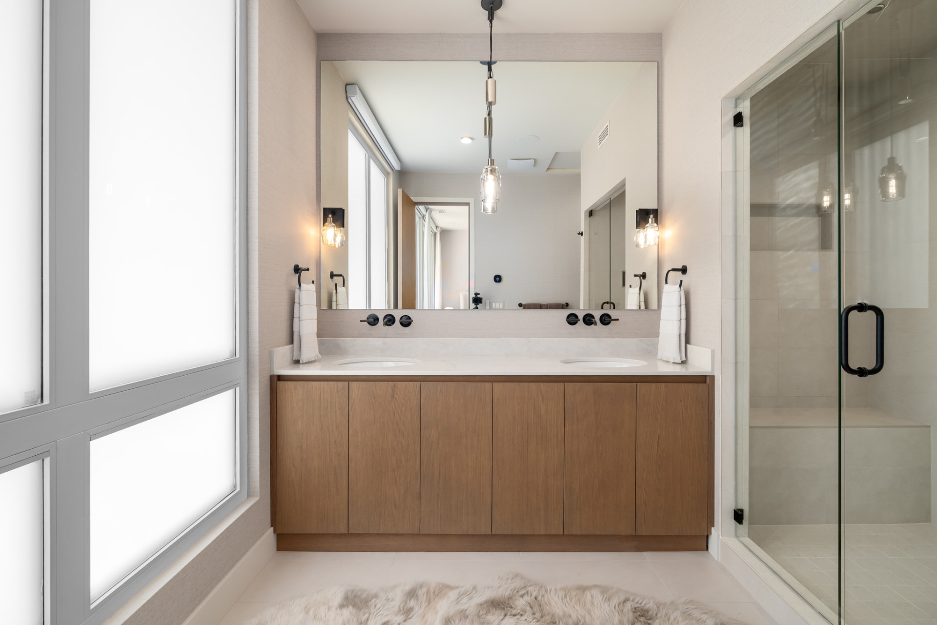 Primary bath with double white oak vanity, marble counters and glass steam shower
