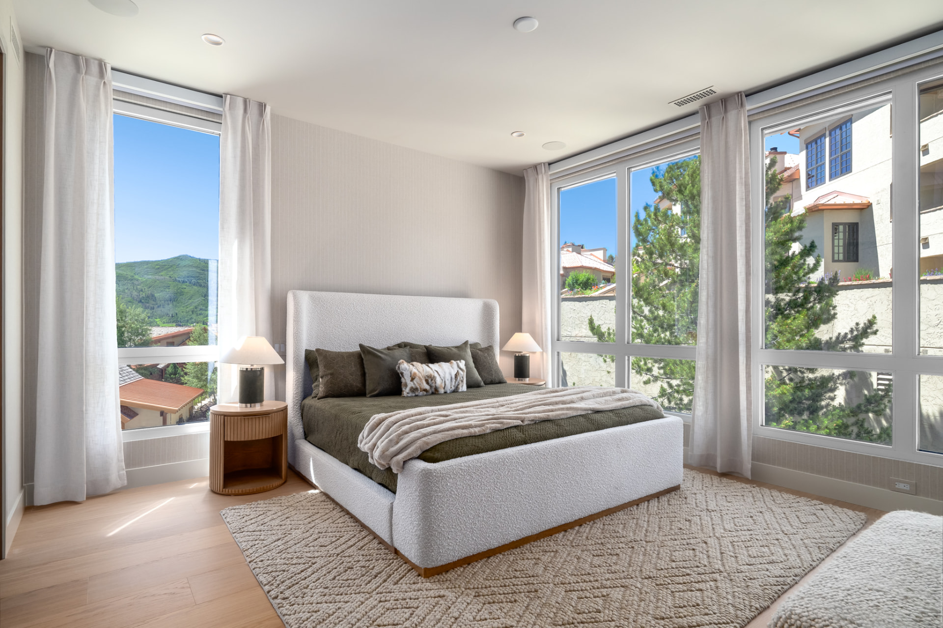 Primary suite with upholstered king bed, layered bedding and mountain views through floor-to-ceiling windows
