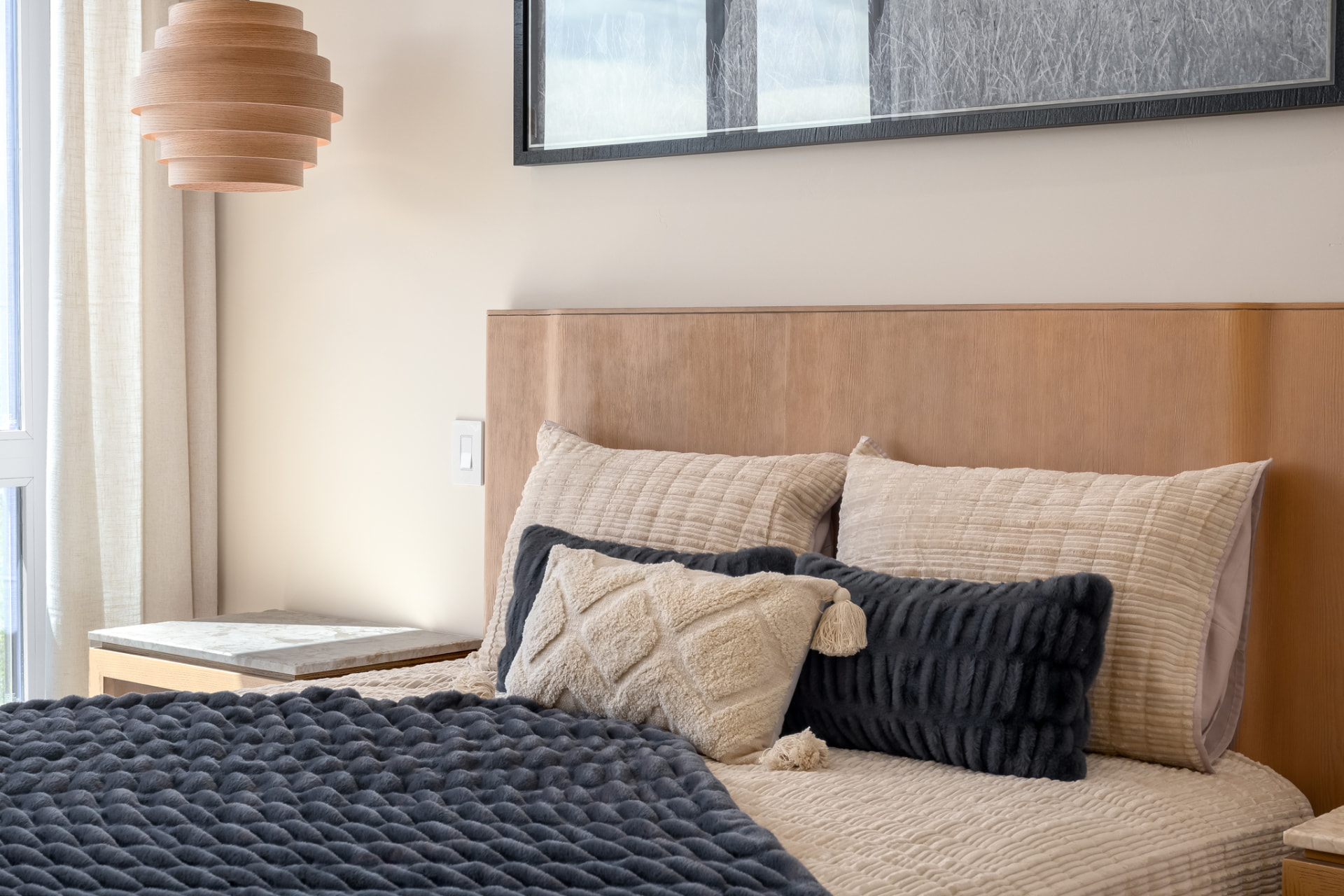 Bedroom detail with white oak headboard, sculptural pendant and layered bedding