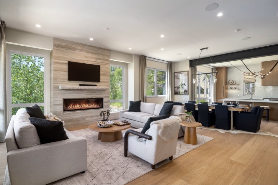 Great room with linear fireplace, media wall, lounge seating and dining area beyond