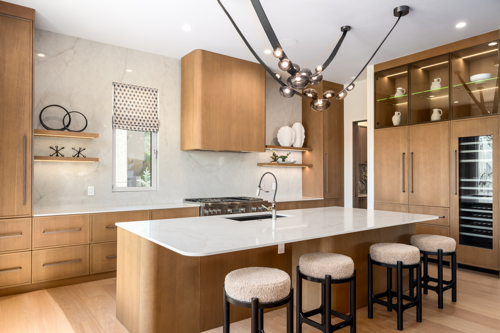 Wide view of the kitchen with wine refrigerator, glass display cabinetry and sculptural chandelier